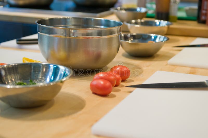 Ripe, fresh tomatoes near a cutting boards, knives and mixing bowls on a kitchen table. Narrow depth of field on tomatoes. Ripe, fresh tomatoes near a cutting boards, knives and mixing bowls on a kitchen table. Narrow depth of field on tomatoes.