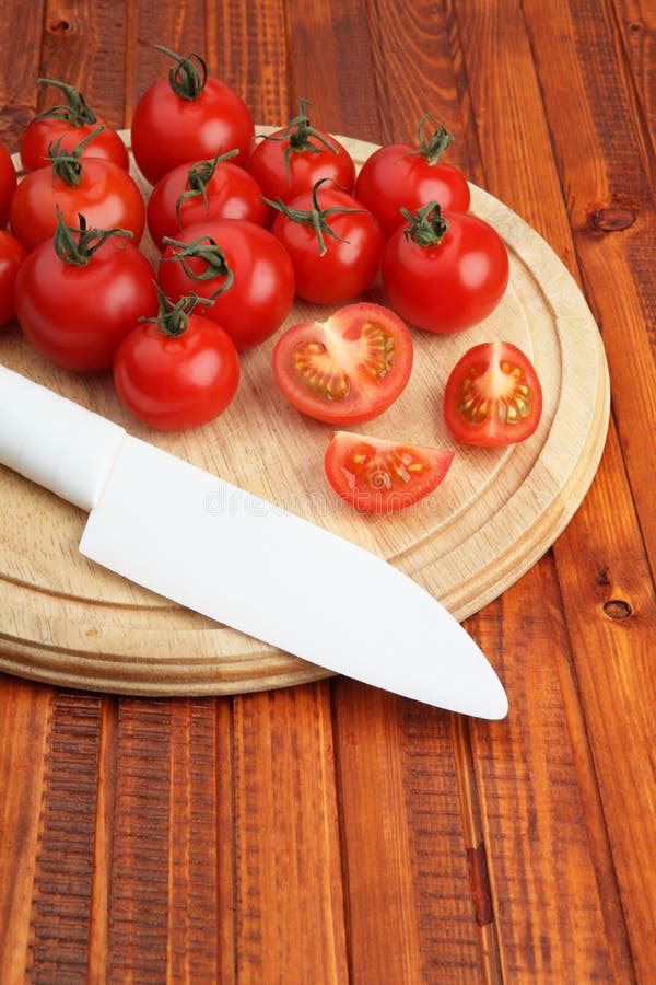Tomatoes on wooden cutting board being cut in half by white knife