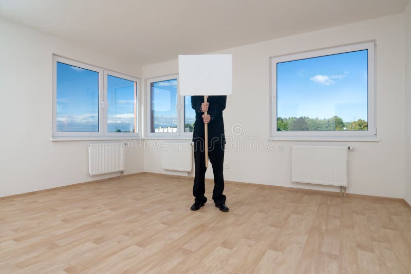 A view of a man standing in an empty or unfurnished room, holding a blank sign on a stick. A view of a man standing in an empty or unfurnished room, holding a blank sign on a stick.