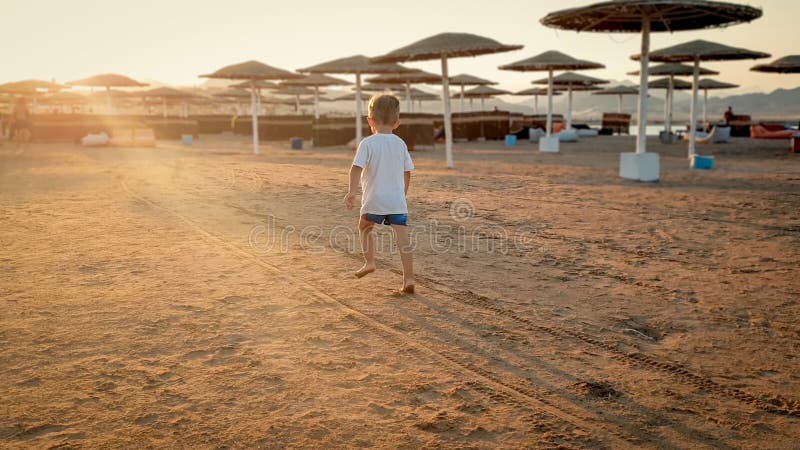 Toned photo of adorable 3 years old toddler boy running on the sea beach towards sunset sun over the shore stock photo Toned photo of adorable 3 years old toddler boy running on the sea beach towards sunset sun over the shore stock photo