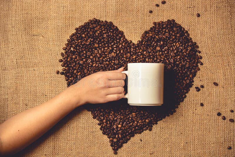 Toned photo of person holding white mug against heart of coffee