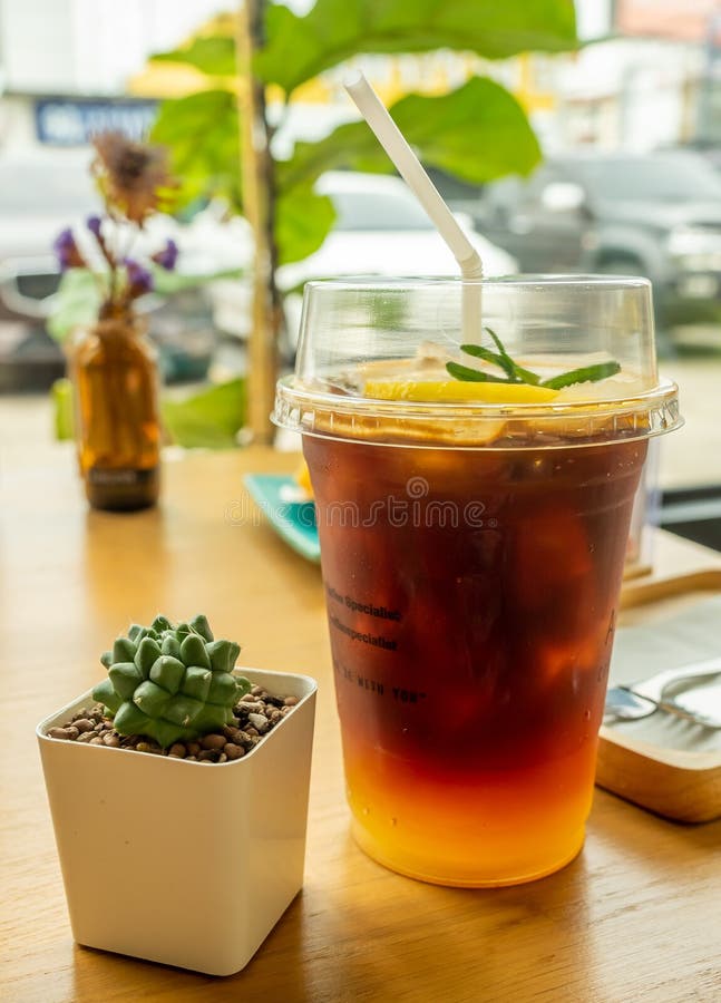 Cold Fruit Tea with a Ice in a Plastic Cup with a Lid on a Wooden