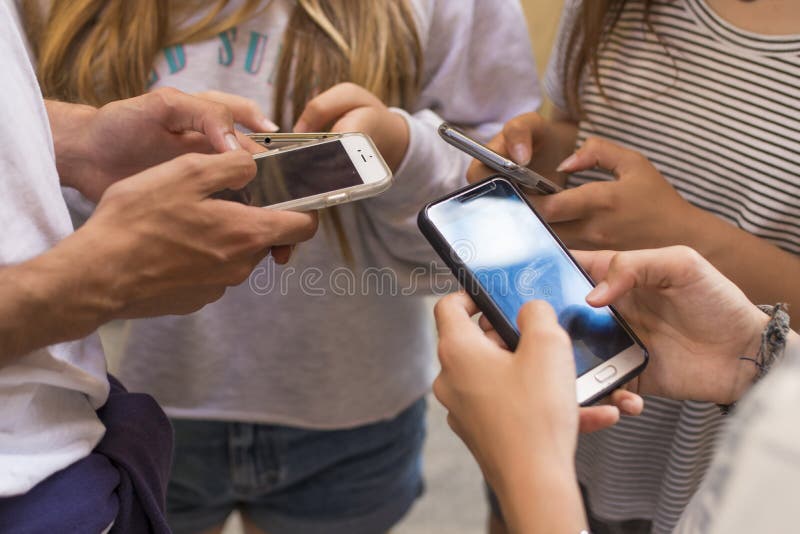 Close up of hands of teens standing outdoors using cell phones. Close up of hands of teens standing outdoors using cell phones.