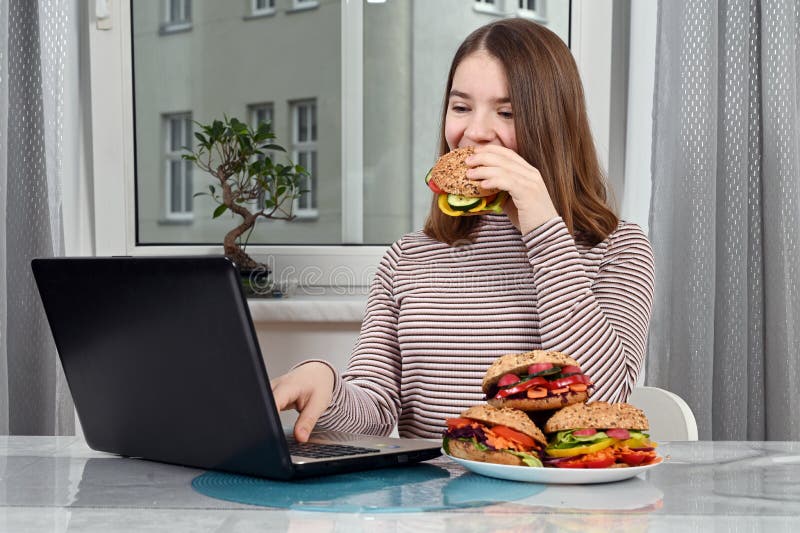 Tonåring som använder en bärbar dator och äter en vegetarisk smörgås fotografering för bildbyråer