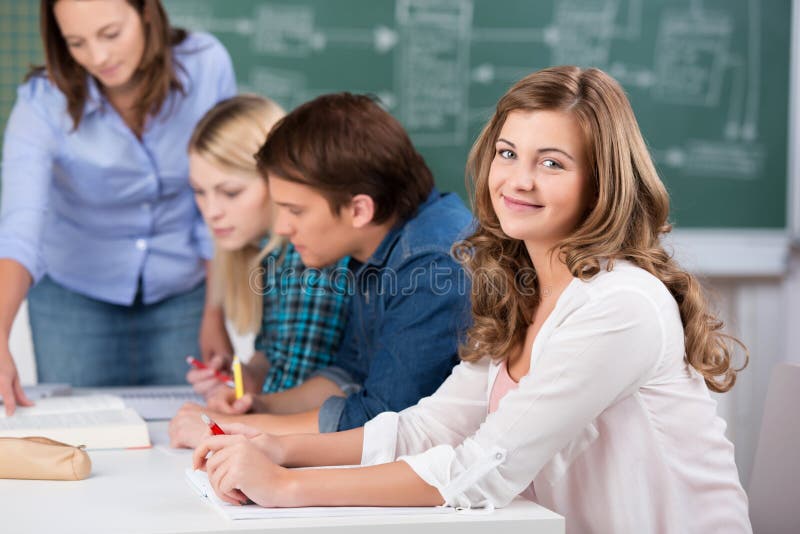 Tonårs- flicka som ler med det lärareAssisting Classmates At skrivbordet