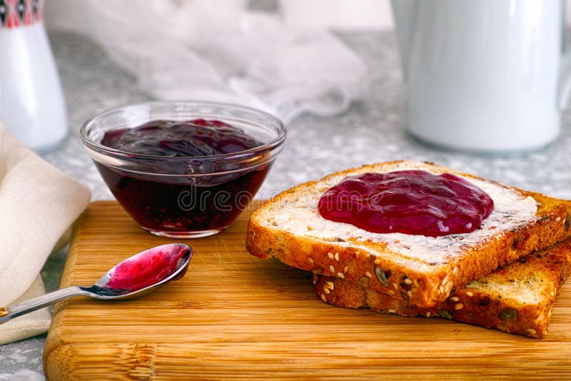 Toosts met jam op houten raad en kom met jam op keukenlijst stock afbeeldingen Toosts met jam op houten raad en kom met jam op keukenlijst stock afbeeldingen