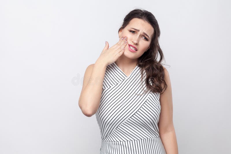 Portrait of sad unhappy beautiful young brunette woman with makeup and striped dress standing touching her chik because feel pain royalty free stock image Portrait of sad unhappy beautiful young brunette woman with makeup and striped dress standing touching her chik because feel pain royalty free stock image