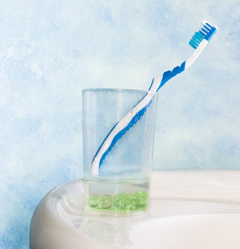 Błękitny toothbrush w szkle dla toothbrushes na obmycie basenie na tle błękit ściana
