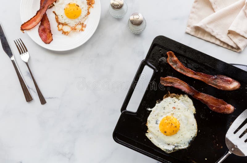 Top Down View of Bacon and Eggs on a Griddle Pan and on a Plate for Breakfast. Stock Image