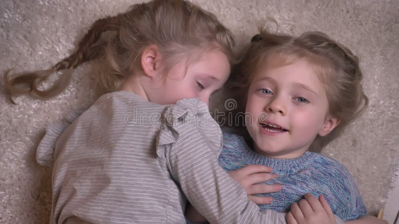 Top Shot Portrait of Two Small Funny Girls Hugging and Kissing Joyfully with Each Other and Lying on the Floor. Stock Video - Video of blonde, braids: 141413543