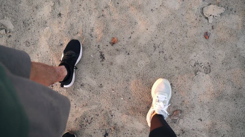 Top-Sicht auf Mann und Frau, die in den Sandstrand des Flusses gehen, in den Turnschuhen. Laufwanderungspaar. pov. stock video footage