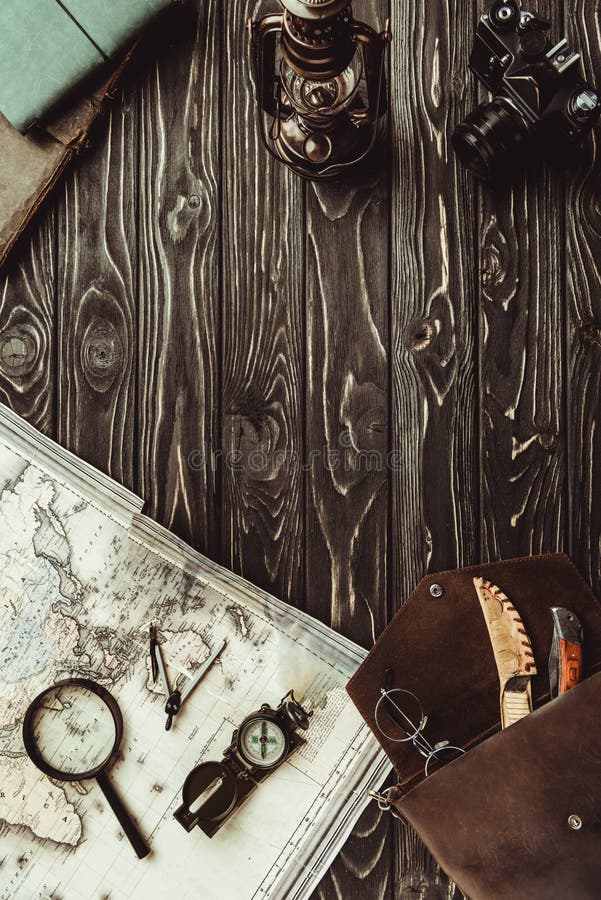 top view of arrangement with map, magnifying glass, bag, compass and retro photo camera on dark