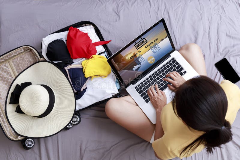 Top view Asian happy woman plan for trip by laptop booking hotel on the bed at home. Women with travel bag use notebook computer