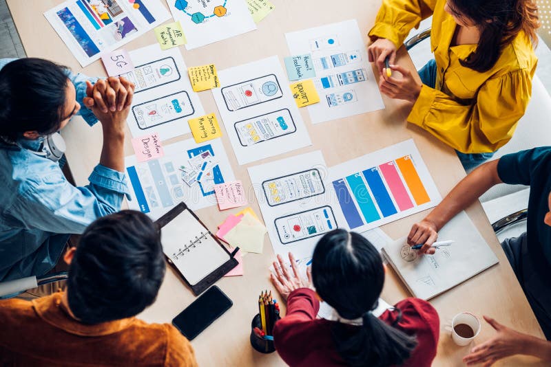 Top view asian ux developer and ui designer brainstorming about mobile app interface wireframe design on table with customer brief