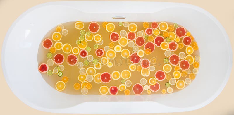 Top view of bathtub filling with water, mixed slices of fresh citrus fruits.