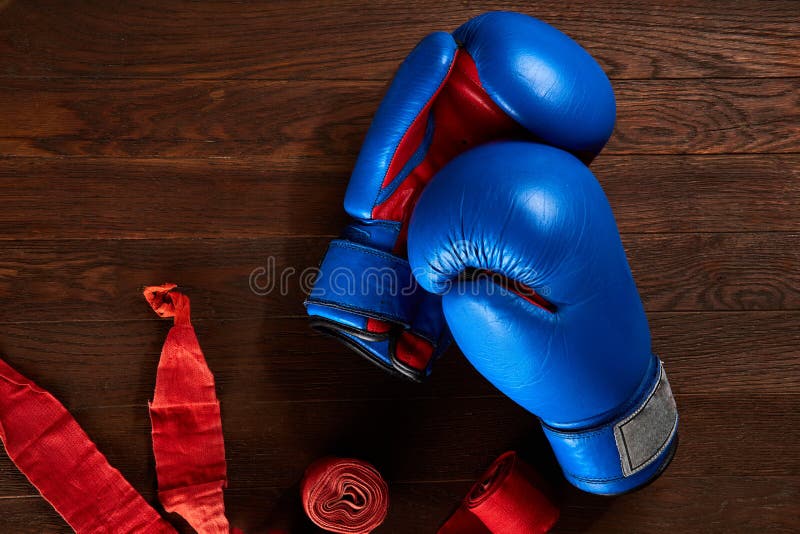 Top view of blue and red boxing gloves and bandage on wooden plank background.