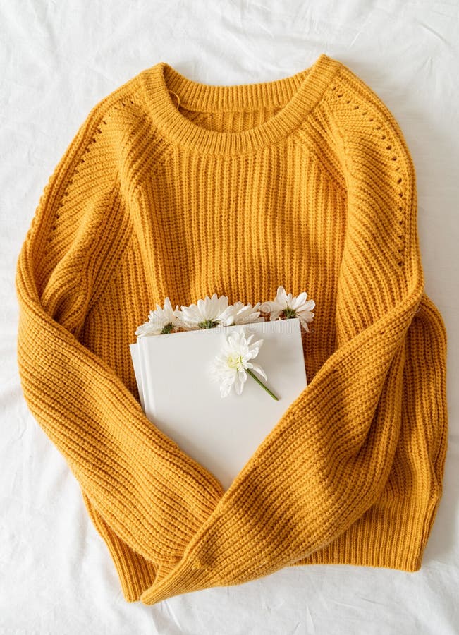 Top view of a book with white chrysanthemum flowers on yellow sweater