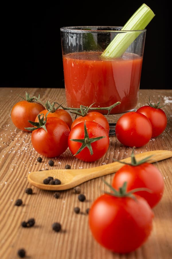 Top view of cherry tomatoes with peppercorns, wooden spoon, glass of tomato juice with celery, selective focus, on wooden table, b