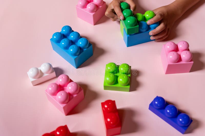 Top view on child& x27;s hands playing with colorful plastic bricks on pink table. Kid building with geometric shapes royalty free stock photos