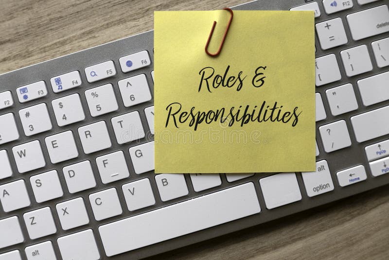 Top view of computer keyboard and yellow memo note with paper clip written with Roles and Responsibilities on wooden background royalty free stock images