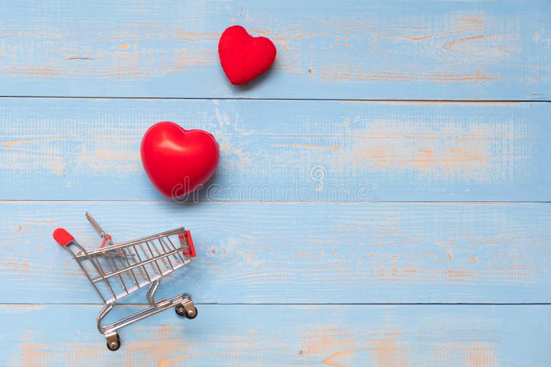 Top view couple red heart shape with mini shopping cart on blue pastel wooden table. love, shopping and Valentine Day Concept