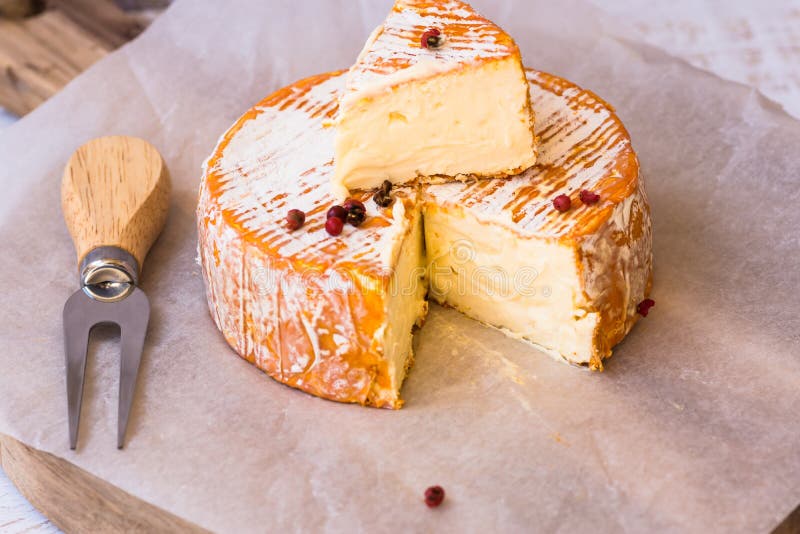 Top view of cut slice of French or German soft cheese with orange rind with mold, creamy texture, red pepper corns, fork royalty free stock photography