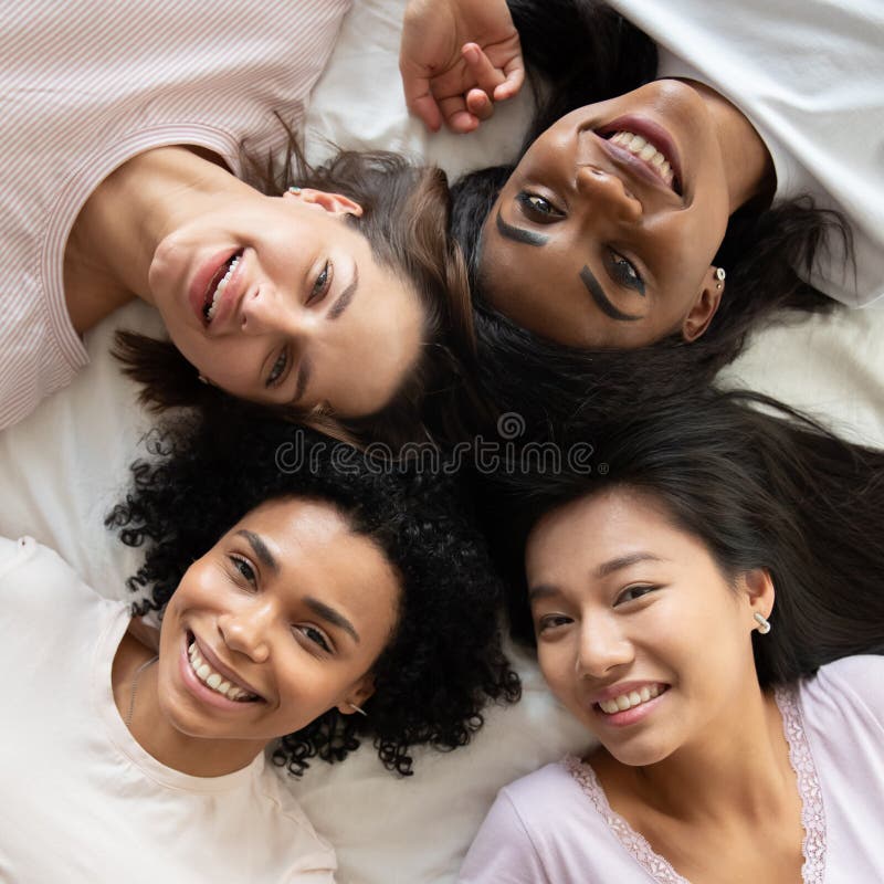 Top view diverse young women friends lying in bed together