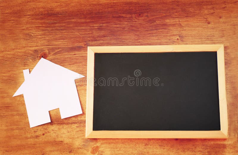 Top view of empty blackboard with room for text and house shaped paper cut over wooden table