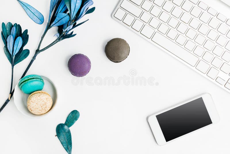 Top view flat lay colorful macarons with keyboard, cell phone and blue leaves on white table. Creative dessert concept royalty free stock images Top view flat lay colorful macarons with keyboard, cell phone and blue leaves on white table. Creative dessert concept royalty free stock images
