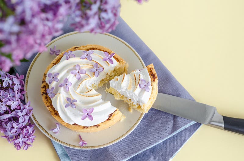 Top view french dessert with lilac flowers. lemon tartlet with italian meringue, whipped cream on a yellow background