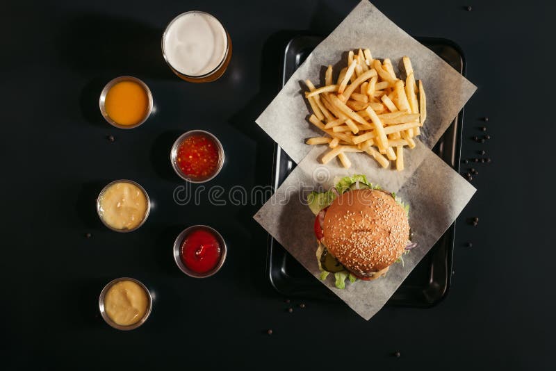 top view of french fries and tasty burger on tray, glass of beer and assorted sauces royalty free stock photography