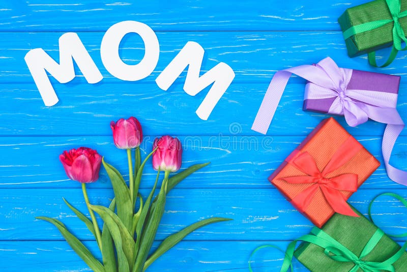 top view of gift boxes, pink tulips and word mom on blue table, mothers day concept