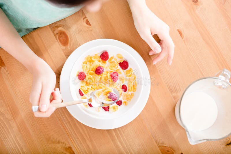 Top view of girl eating cereals with strawberry and milk