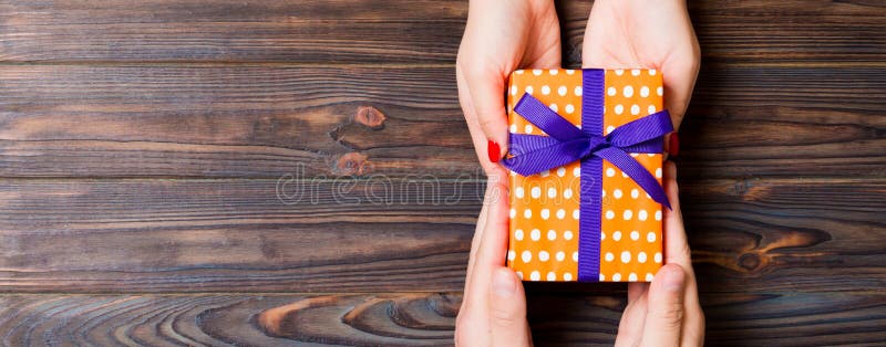 Top view of giving and receiving a gift on wooden background. Present in male and female hands. Love concept. Copy space