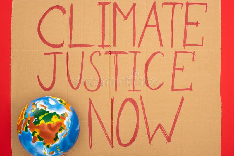 Top view of globe and placard with climate justice now lettering on red background, global warming concept