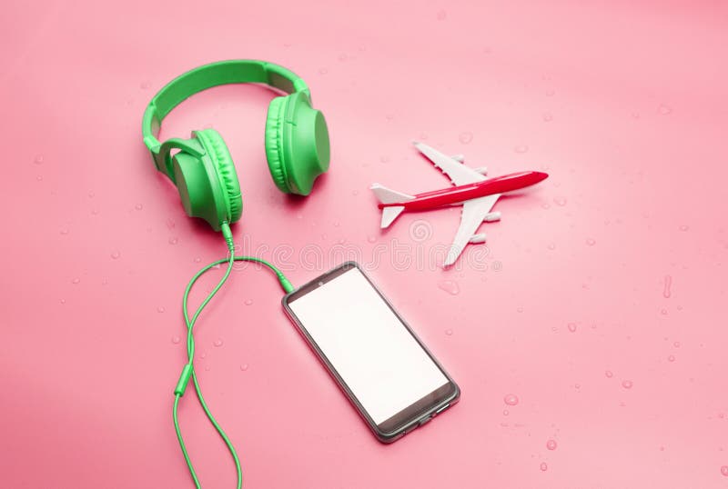 Top view Green overhead music headphones in water drops, with travel airplane, copy space. Headphones on a pink pastel background royalty free stock photo