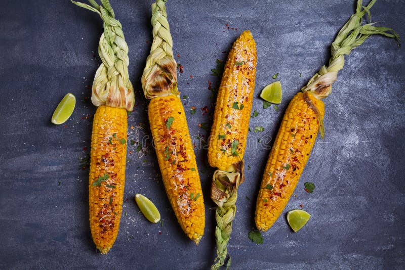 Top view of grilled sweet corn cob with parmesan cheese, paprika, salt, cilantro and lime.