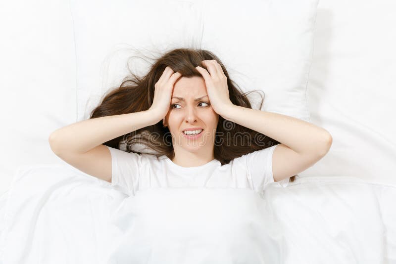 Top view of head of tired brunette young woman lying in bed with white sheet, pillow, blanket. Shocked female cover ears stock photography Top view of head of tired brunette young woman lying in bed with white sheet, pillow, blanket. Shocked female cover ears stock photography