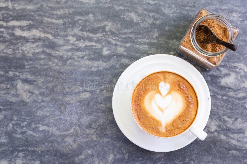Top view of hot coffee with heart pattern in white cup and brown sugar on stone table background royalty free stock photo Top view of hot coffee with heart pattern in white cup and brown sugar on stone table background royalty free stock photo