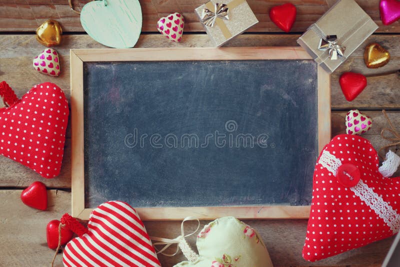 Top view image of colorful heart shape chocolates, fabric hearts, gift boxes and chalk board on wooden table