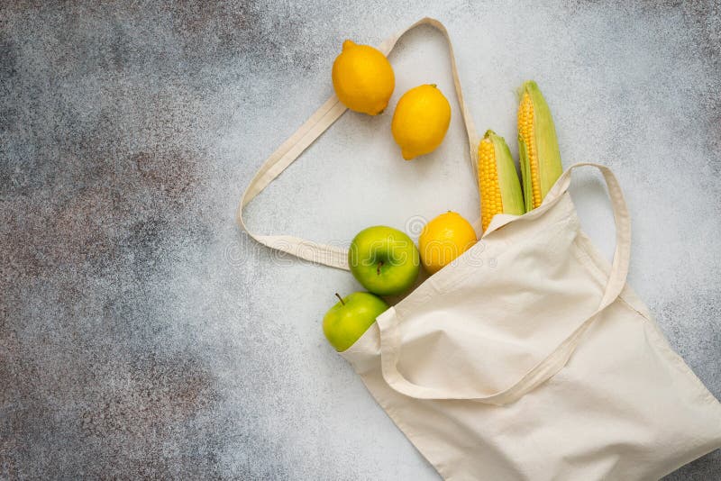 Top view of lemons, apples and corn. Vegetables and fruits in eco shopping bag on the concrete background.