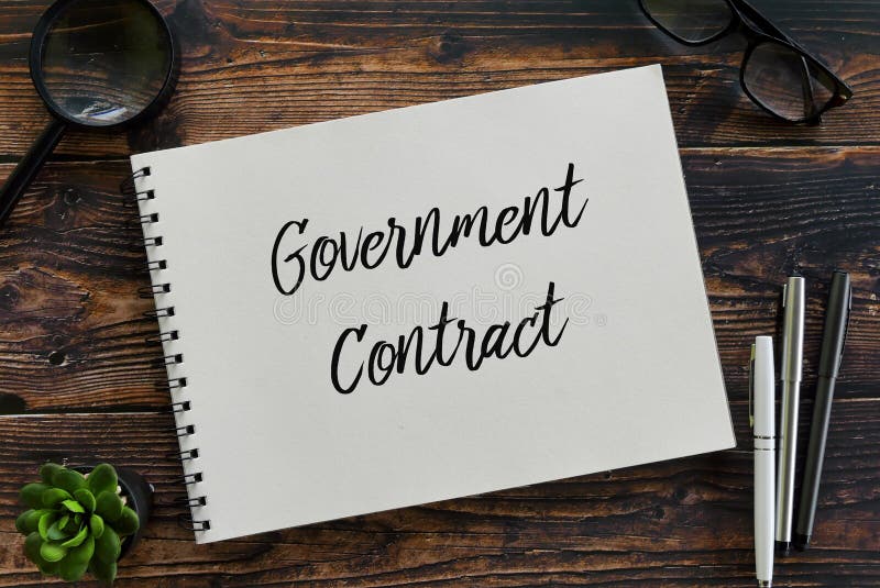 Top view of magnifying glass,glasses,pen,plant and notebook written with Government Contract