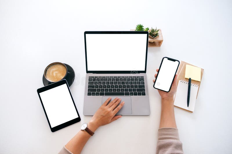 Hands holding a blank white screen mobile phone with laptop computer and tablet pc on the table in office stock images