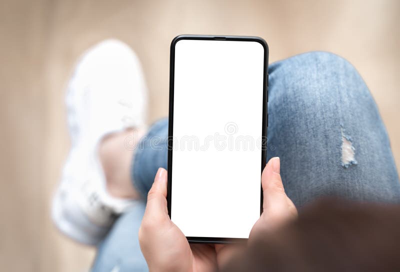 Top view mockup image of woman holding mobile phone with blank white screen. Woman in jeans sits cross-legged and holds cell phone royalty free stock photo
