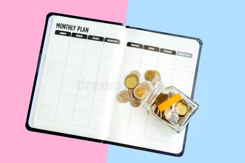Top View money bottle with saving yellow label placed on the blank monthly plan notebook, coins spilling out isolated on white bac stock photo Top View money bottle with saving yellow label placed on the blank monthly plan notebook, coins spilling out isolated on white bac stock photo