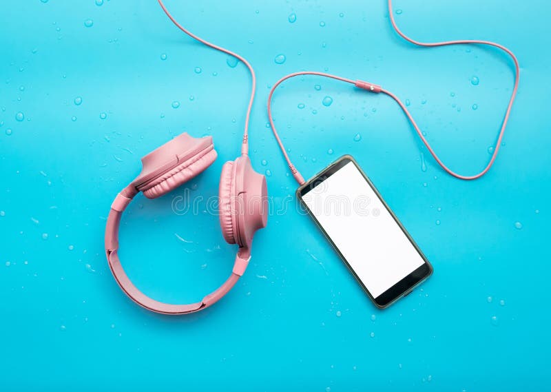Top view, Music headphones in water drops, smartphone with white display for text or playlist, copy space. Headphones on a blue stock image