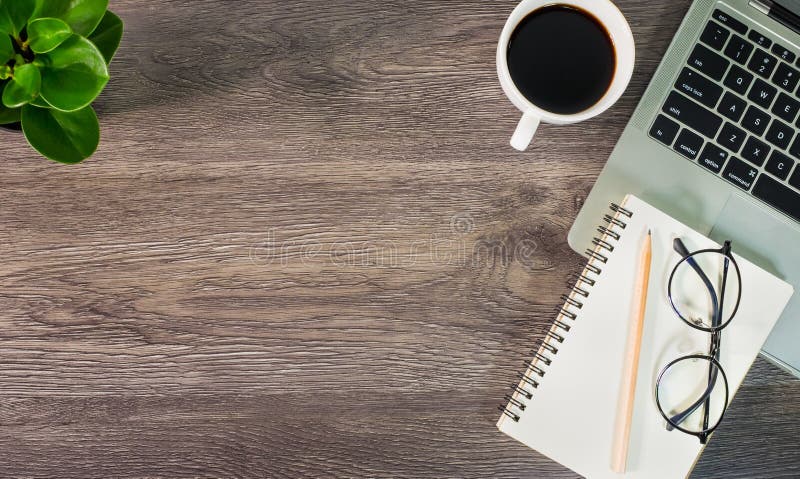 Top view of Office desk wooden table with laptop notebook, pencil, glasses and white cup of black coffee.