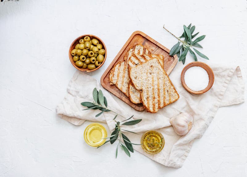 Top view olive oil, olives, toast bread and leaves on white background