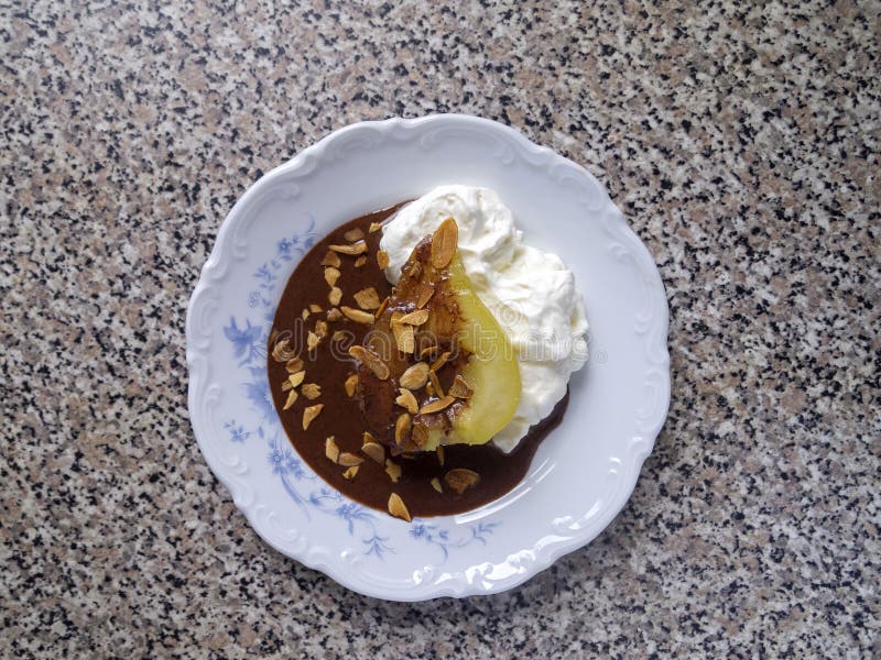 Top view of one poached caramelized pear with whipped cream, chocolate sauce and almond flakes