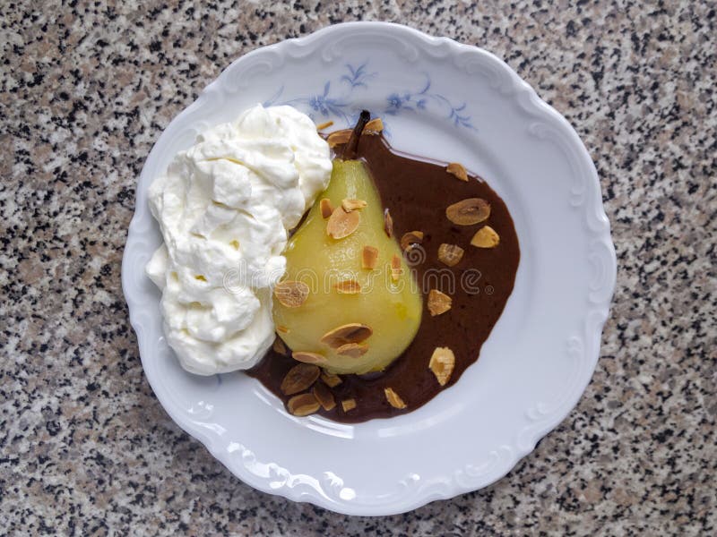 Top view of one poached caramelized pear with whipped cream, chocolate sauce and almond flakes